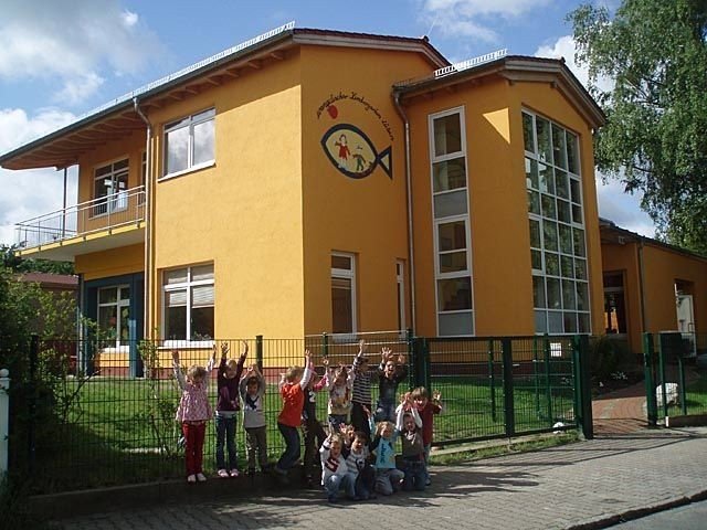 Außenansicht der Kita Lübars von der Straße aus, vor dem Zaun steht eine Kindergruppe.